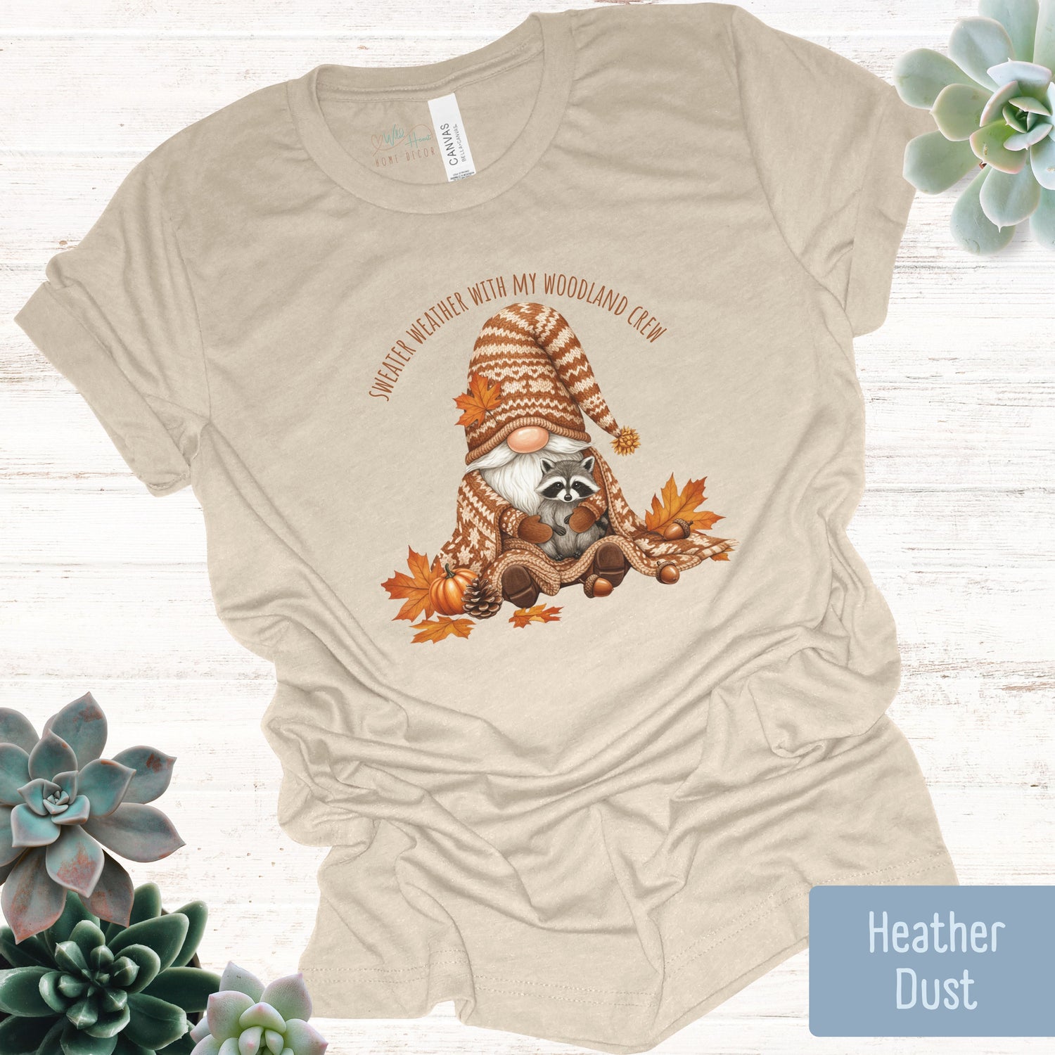 Beige t-shirt with a raccoon gnome graphic and text on a white background with succulents.